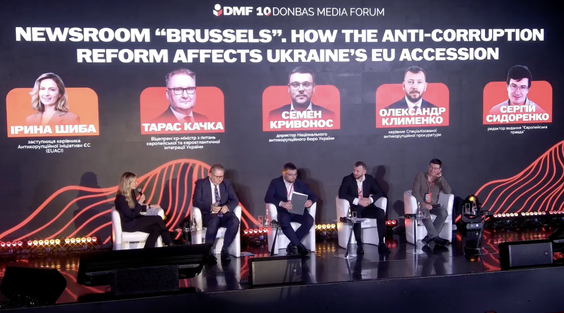 Five panelists sit in white chairs on a stage at the Donbas Media Forum 10, participating in a discussion titled "Newsroom 'Brussels': How the Anti-Corruption Reform Affects Ukraine's EU Accession." The stage features red lighting effects and displays headshots of the speakers, including Iryna Shyba, Taras Kachka, Semen Kryvonos, Oleksandr Klymenko, and Serhii Sydorenko, with their titles in Ukrainian text.