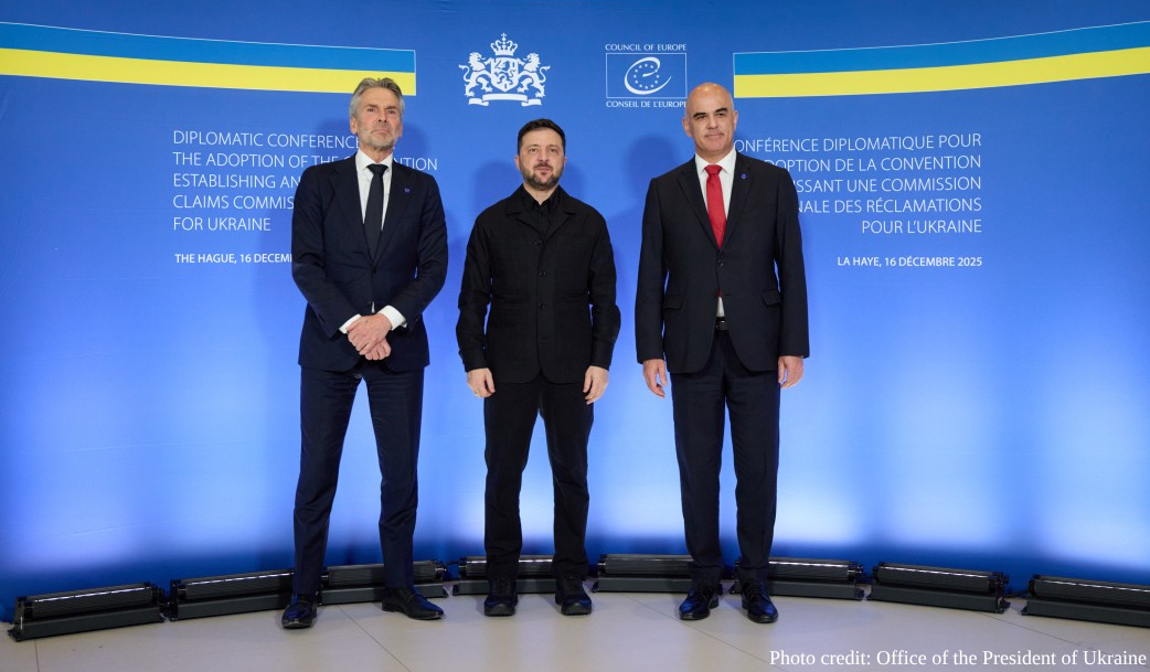 Three men in dark business suits stand side by side in front of a blue backdrop with Council of Europe logos and Ukrainian flag colors, at a diplomatic conference in The Hague on Dec. 16, 2025, regarding the adoption of a convention establishing an international claims commission for Ukraine.