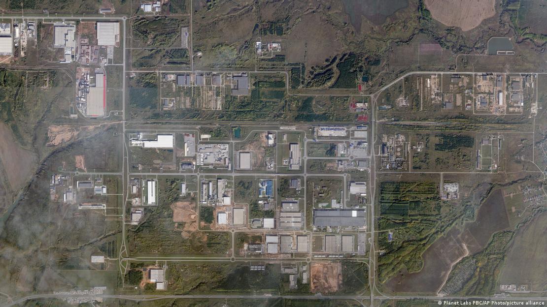 An aerial satellite view shows an industrial zone in Bashkortostan, Russia, with multiple warehouse and factory buildings arranged in a grid pattern among roads and undeveloped land. The image, credited to Planet Labs PBC/AP Photo/picture alliance, displays various commercial and industrial structures surrounded by open terrain.