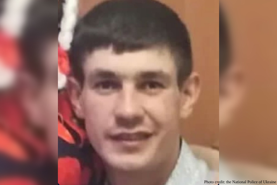 A young man with short dark hair and a subtle smile looks directly at the camera in a close-up portrait. The image shows him in casual attire with red elements visible in the blurred background.