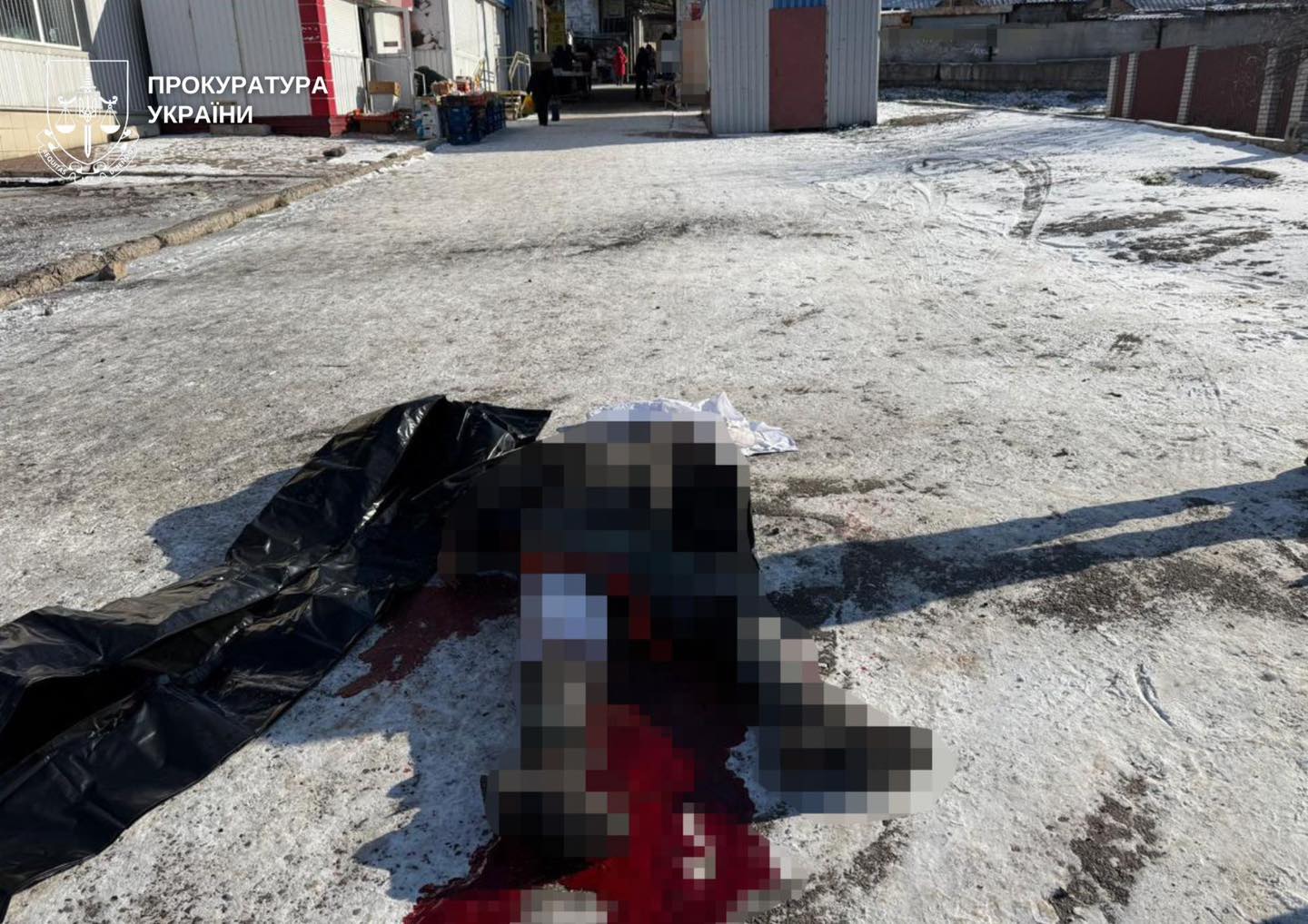A wide shot of an outdoor market area covered in light snow. In the foreground, one body is completely covered by a black tarp, and another pixelated body lies nearby with visible blood on the ground. Empty market stalls are in the background.