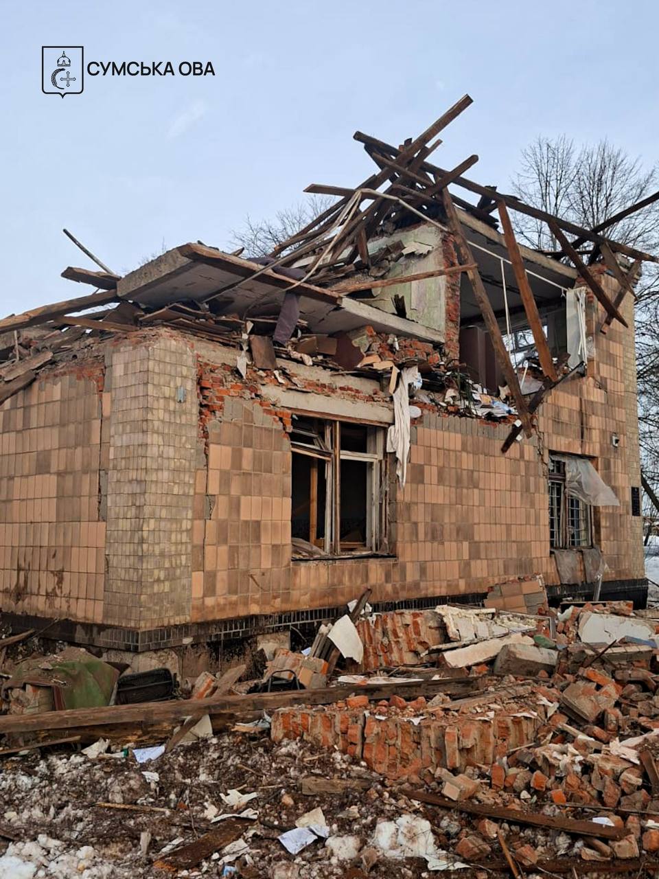A heavily damaged two-story building in the Yampil community of the Sumy region is shown with a completely collapsed roof and shattered exterior tiled walls. The "СУМСЬКА ОВА" (Sumy OVA) logo is in the top-left corner, documenting the aftermath of a Russian drone strike on an agricultural enterprise on February 27, 2026.