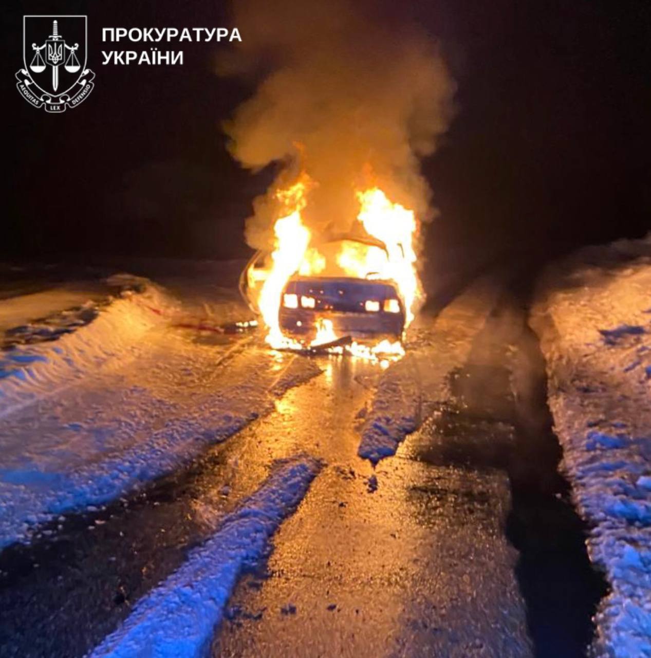 A blue civilian car is engulfed in bright orange flames on a snow-covered road at night following a Russian drone strike in the Vorozhba hromada of the Sumy region, Ukraine, on February 27, 2026.