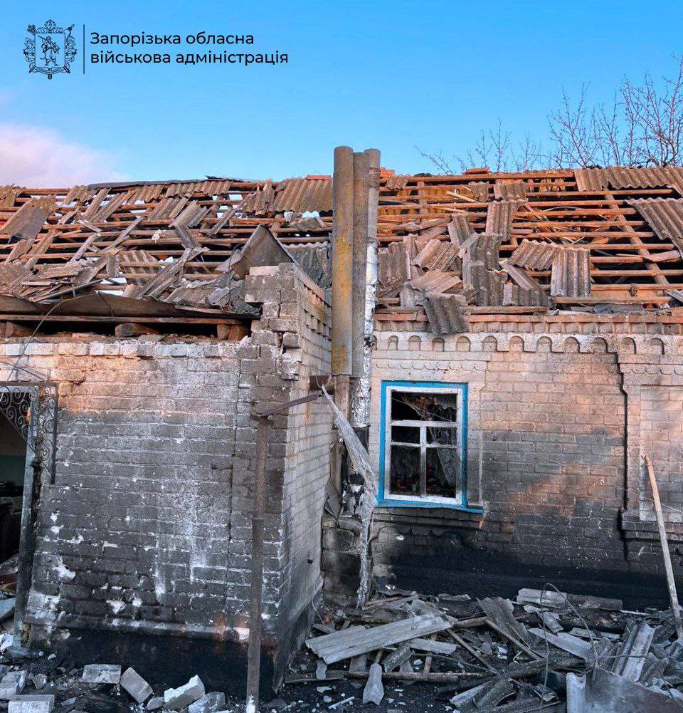 Alt-text Generator Custom Gem Alt-text Generator said A one-story brick house shows severe damage, with its slate roof largely destroyed and the wooden rafters exposed. The facade is charred with soot, a window with a blue frame is missing its glass, and debris is scattered on the ground in the foreground.