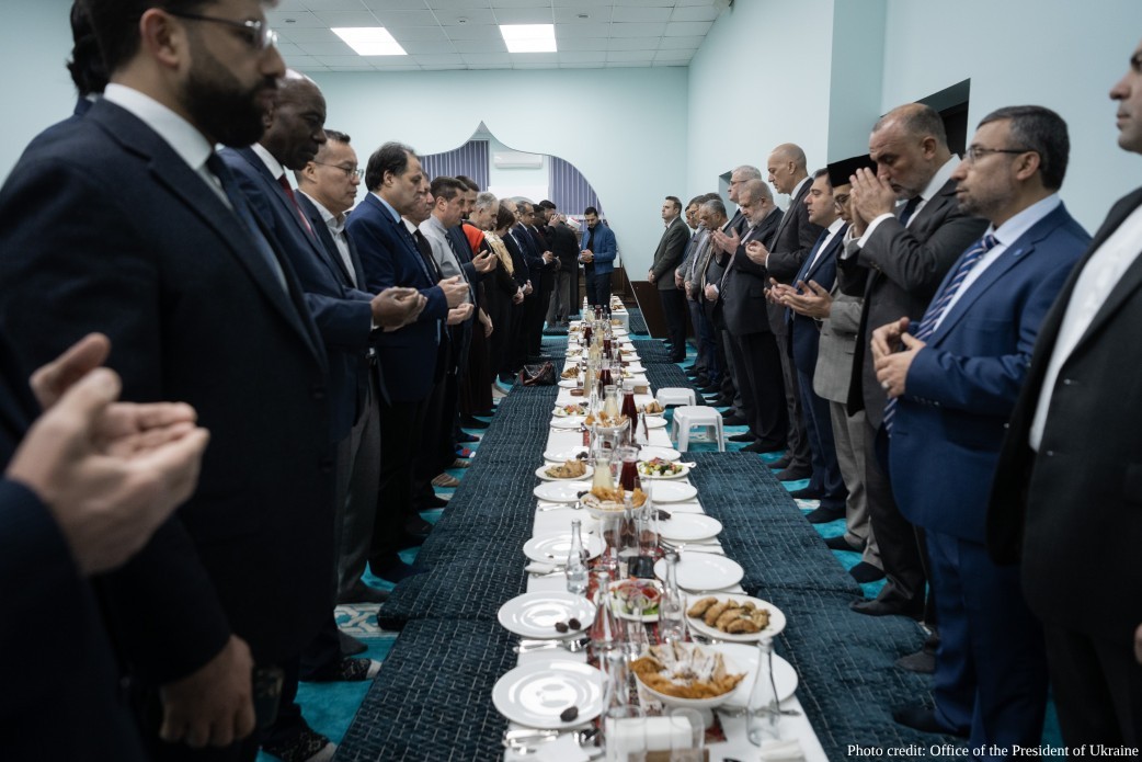 President Volodymyr Zelenskyy and senior Ukrainian officials (including Kyrylo Budanov, Rustem Umerov, and Andrii Sybiha) stand in prayer alongside Muslim military personnel and community leaders during an Iftar ceremony in Kyiv on March 2, 2026. The long table is set with traditional dates and water, and the event was held on the grounds of the Spiritual Administration of Muslims of Crimea to honor warriors of the Islamic faith.