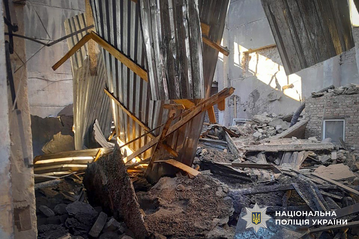 The interior of a destroyed building shows twisted metal siding and wooden supports hanging over a floor covered in large chunks of concrete and rubble. The National Police of Ukraine logo is visible in the bottom right corner.