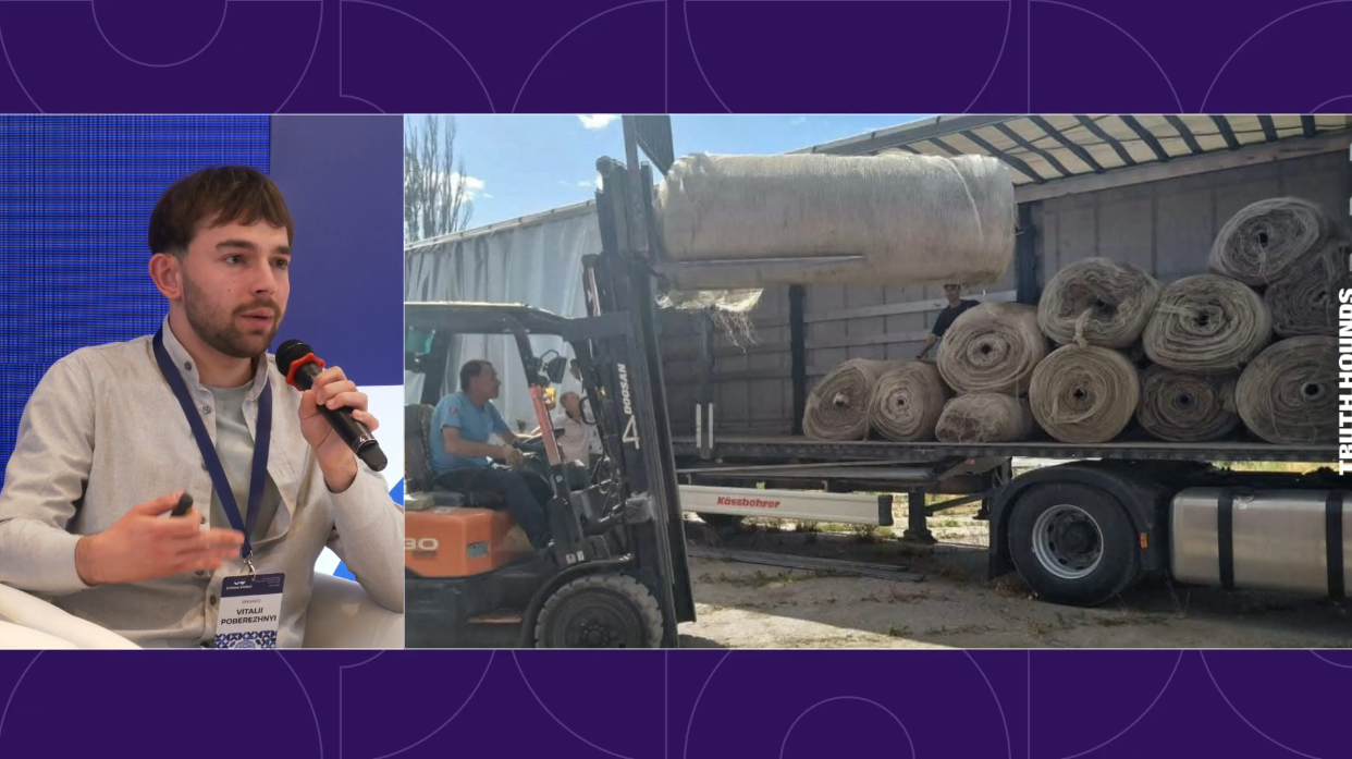 A split-screen presentation shows a man on the left speaking into a microphone during a conference. On the right, a video still shows a forklift operator loading large, wrapped rolls of material onto the back of a flatbed semi-trailer.