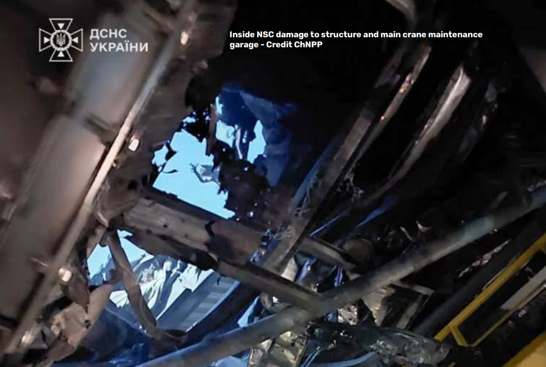 A low-angle, interior photograph shows severe structural damage to the New Safe Confinement (NSC) at the Chernobyl Nuclear Power Plant. Jagged, mangled metal beams and debris frame a large hole in the roof, through which a clear blue sky is visible. Text in the upper-right corner reads "Inside NSC damage to structure and main crane maintenance garage - Credit ChNPP," while the State Emergency Service of Ukraine (DSNS) logo appears in the top-left corner.
