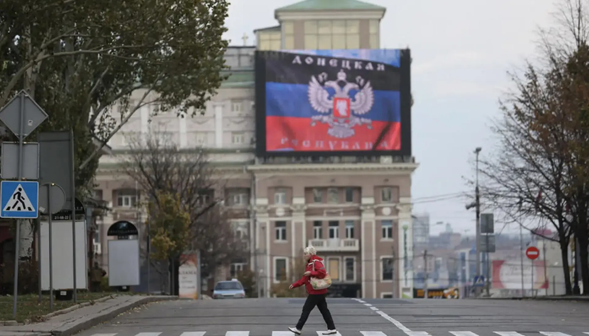 Людина переходить порожню вулицю в окупованому Донецьку, а на великому екрані будівлі демонструють прапор самопроголошеної "ДНР".